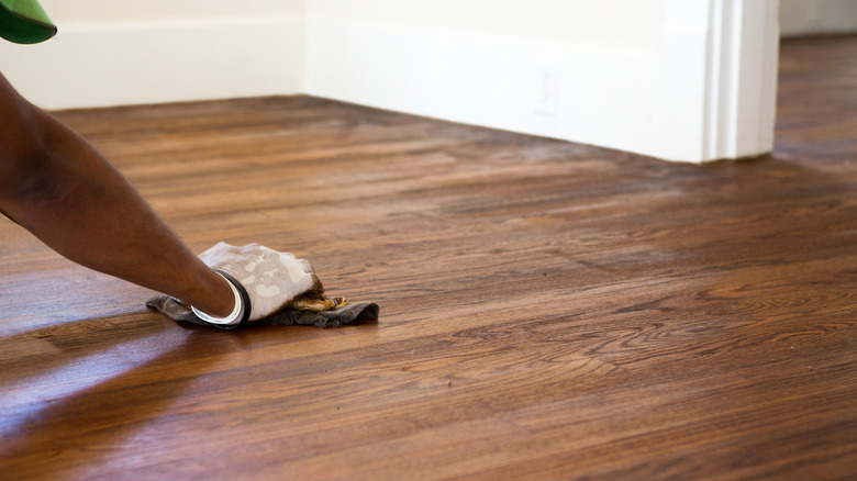 An arm is shown running a cloth over a newly stained hardwood floor