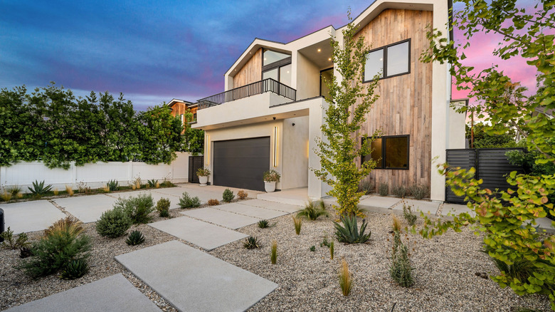 Beige gravel lines the yard of a beige and wood toned house