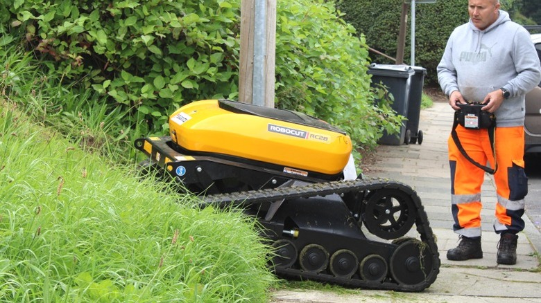 Man operating large remote control lawn mower up steep hill