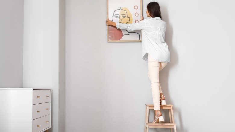 Woman on step stool hanging picture