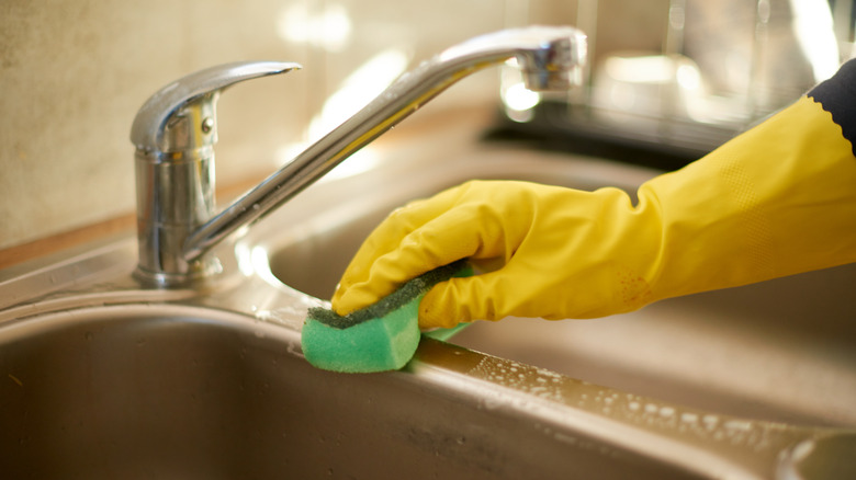 A person wearing yellow rubber gloves cleaning a kitchen sink