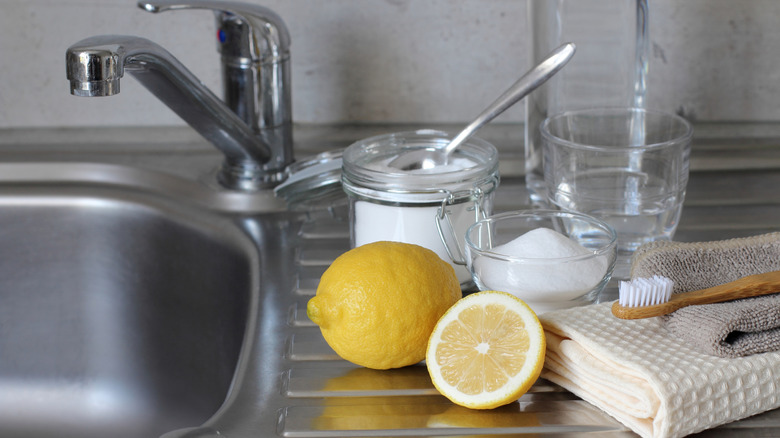 A collection of natural cleaning products, including baking soda and vinegar, by a sink