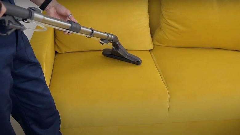 A man uses a vacuum to clean a yellow velvet sofa