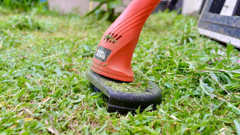 A Black+Decker weed eater in use, covered in grass clippings