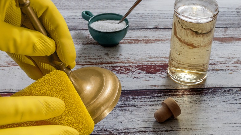 Gloved hands cleaning a brass candlestick with salt and vinegar