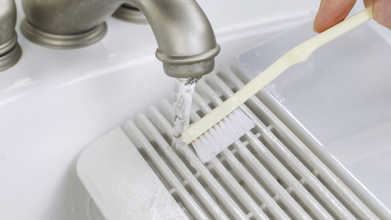 Person scrubbing a vent cover in the sink with a toothbrush