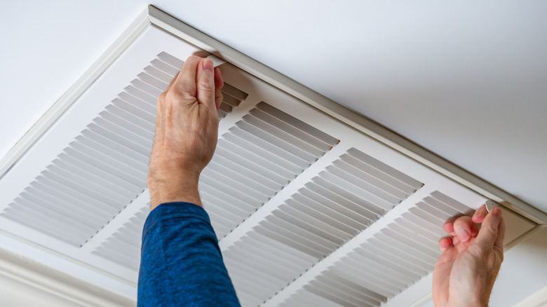 Person opening white ceiling vent cover