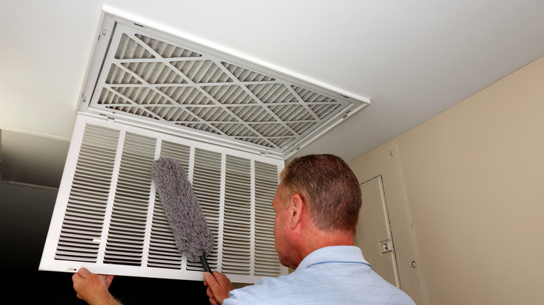 Man dusting ceiling vent cover