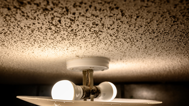 A close up of a popcorn ceiling covered in black dust and a light fixture.