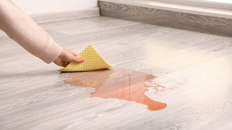 Person using a cloth to wipe spilled wine on a hardwood floor