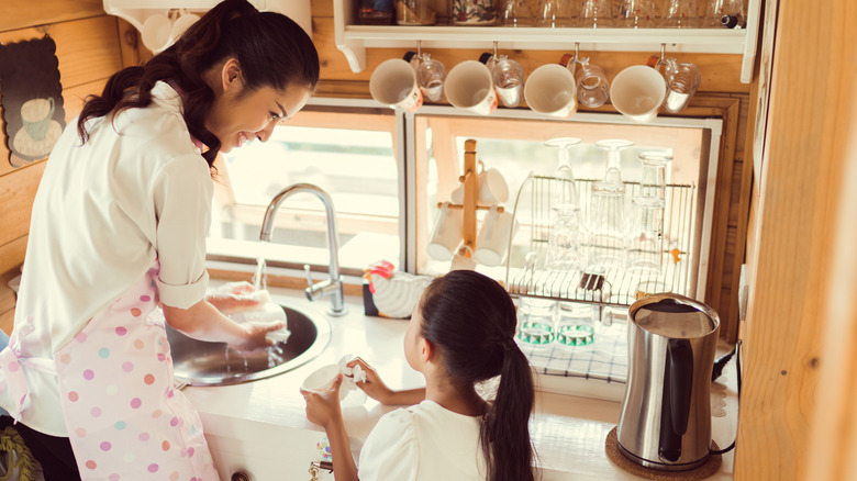 woman washing dishes with child