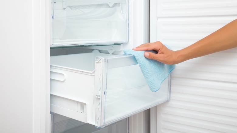 person wiping fridge drawer with rag