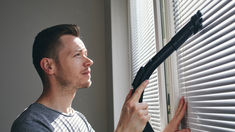 Man cleaning blinds with vacuum