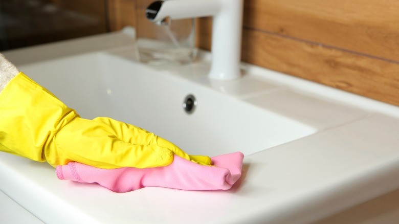 Yellow gloved hand cleaning sink