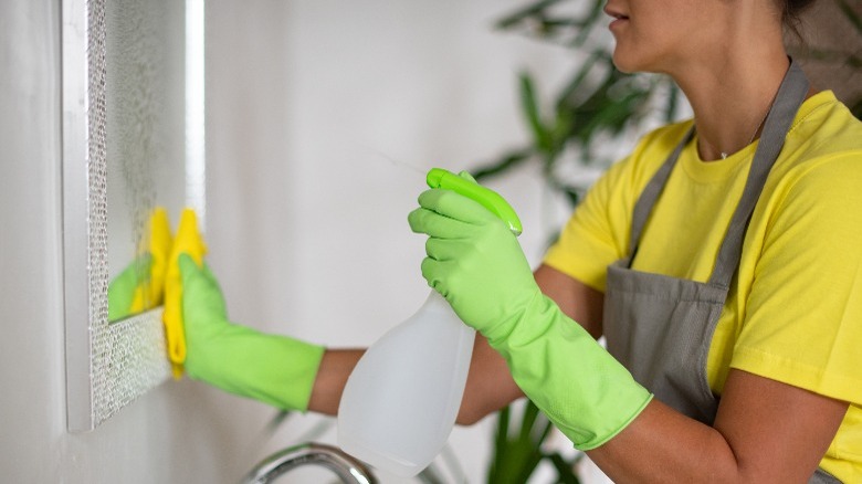 Woman wearing green gloves cleaning mirror