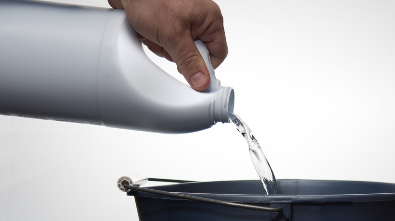 Hand pouring bleach from bottle into a bucket