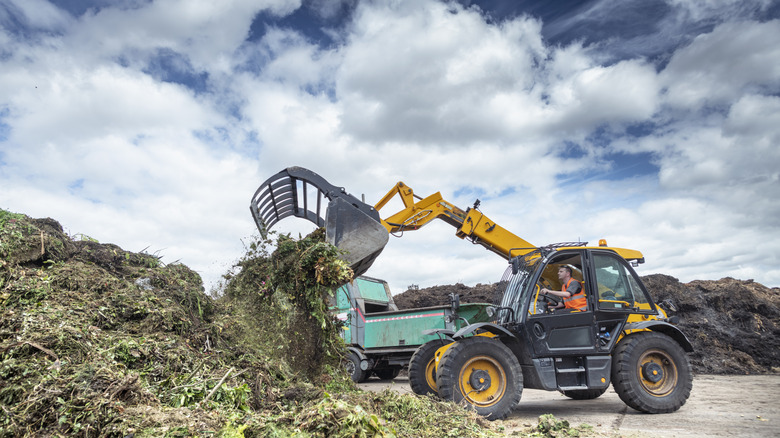 A worker in a claw excavator mixes a compost heap