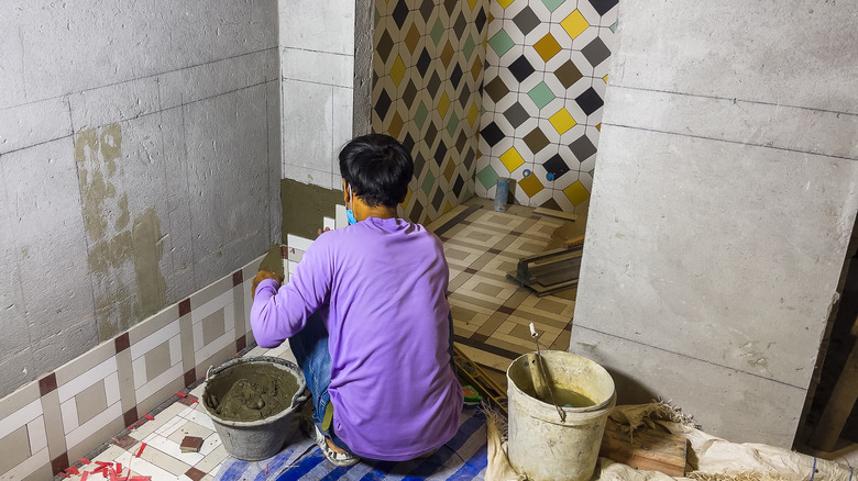 A person installs patterned tile in a bathroom