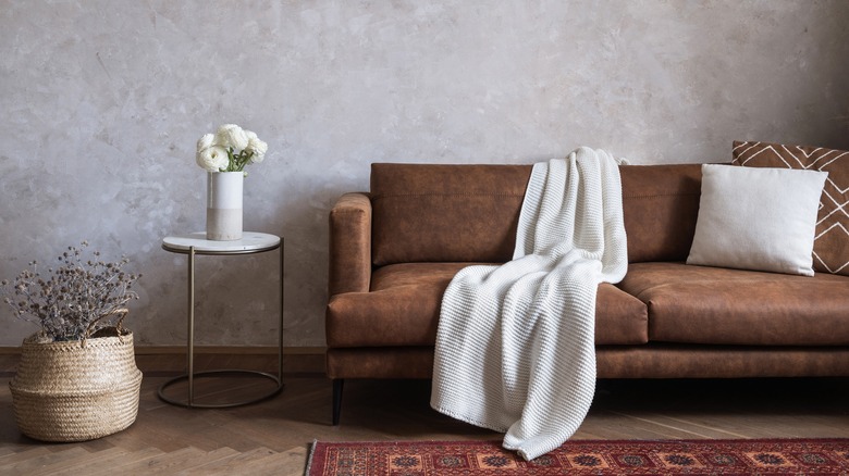 Plaster effect gray wall, suede sofa, marble and steel side table, and waffle-weave blanket