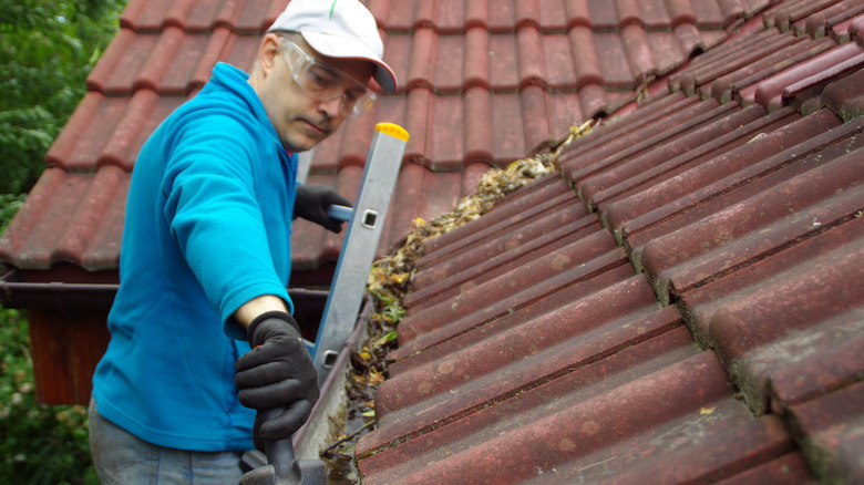 man cleans roof gutters