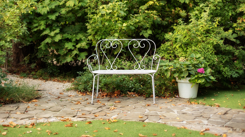 a white, wrought-iron garden bench outdoors