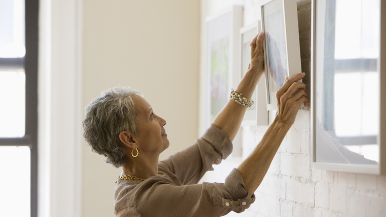 woman hanging artwork on painted brick wall