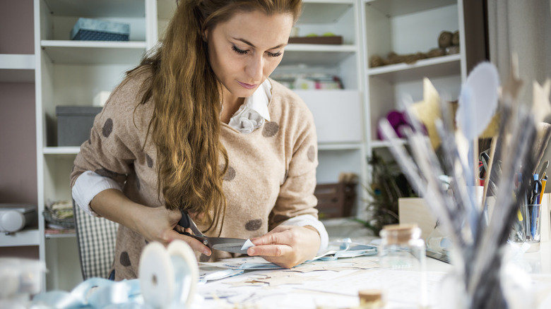 A woman crafts at a table, with arts and crafts supplies nearby