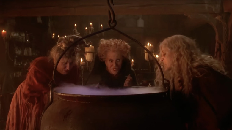 The Sanderson sisters huddle over a bubbling cauldron.