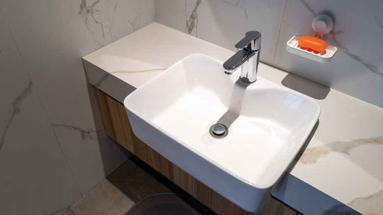 White bathroom sink jutting out of countertop and soap dish above