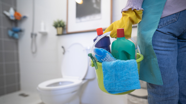 Person holding a bucket of cleaning supplies in a bathroom