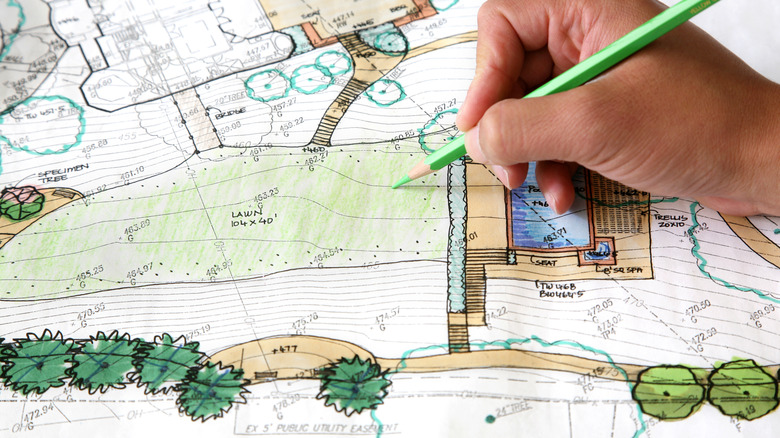 A person is drawing a garden design plan on drafting paper