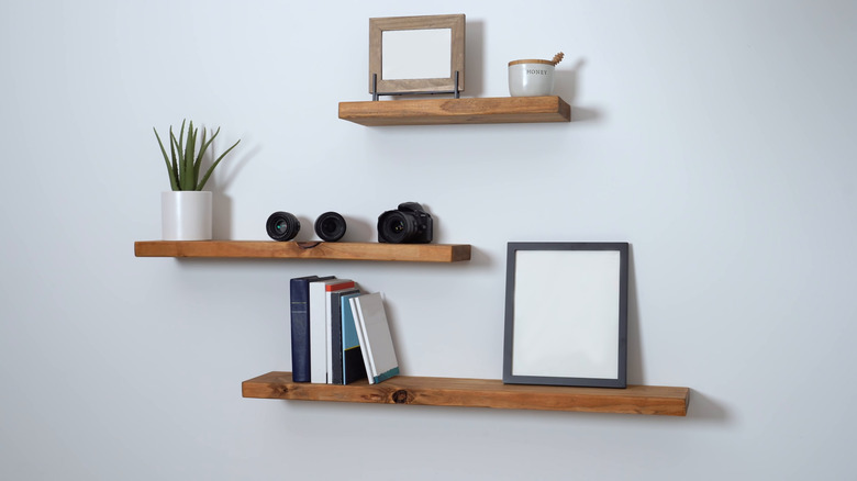 Three wood floating shelves house small plants and a few books as well as small decorative items.