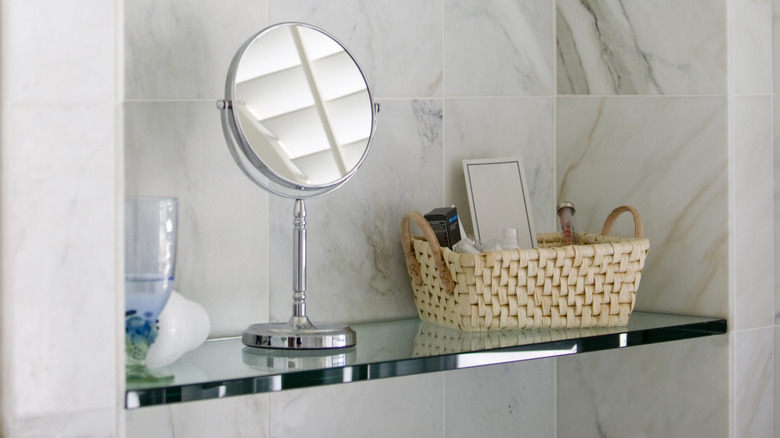 A mirror and a wicker basket rest on a glass floating shelf