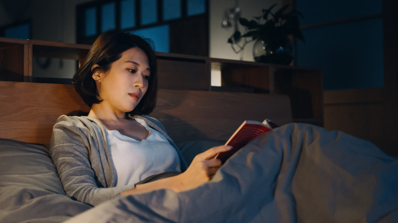 Asian woman in reclined position reading a book at night