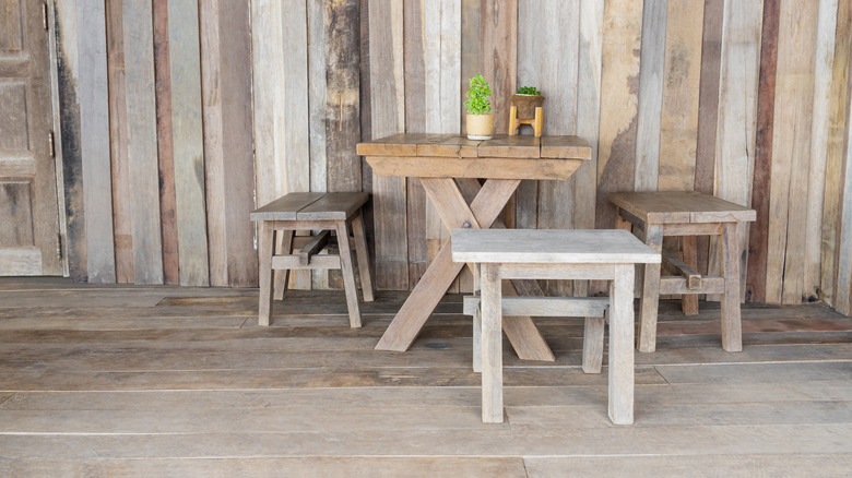 A set of basic wooden furniture is housed within a space full of distressed wood walls and floor planks.