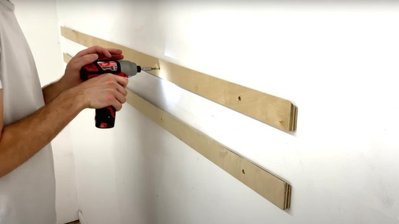 Man drilling plywood French cleat into garage drywall over another cleat