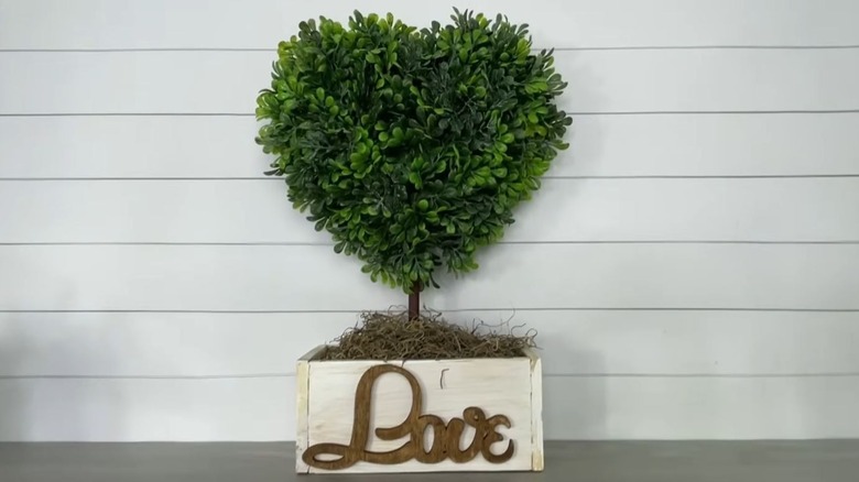 A faux heart topiary rests in a small wooden box with "Love" written on the front.