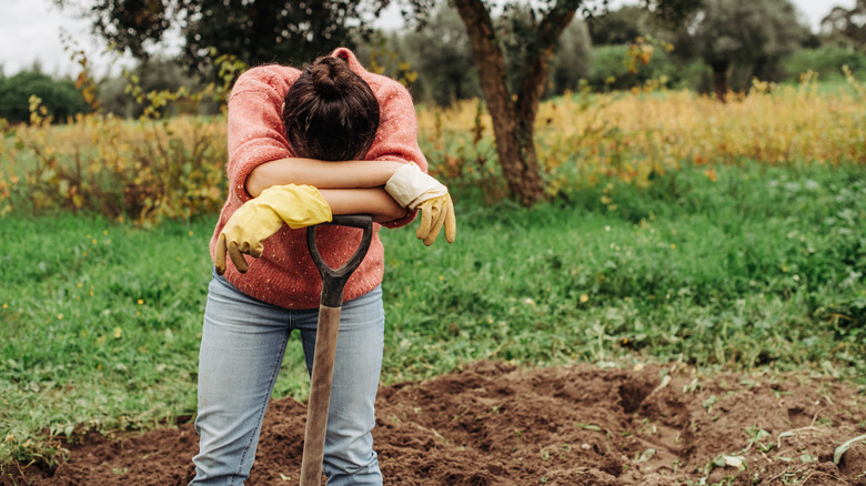 person leaning head on shovel