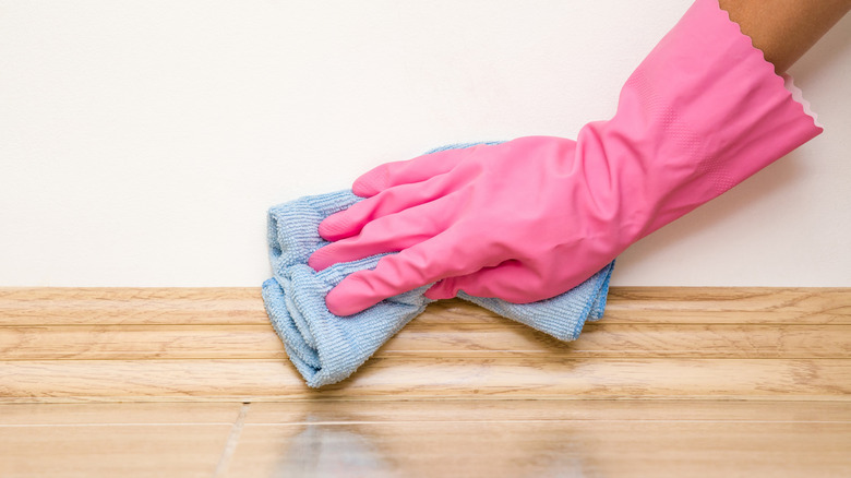 Pink gloved hand wiping baseboards