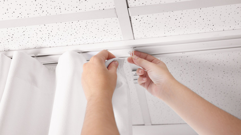 female hand hanging white drapes on ceiling curtain track rollers