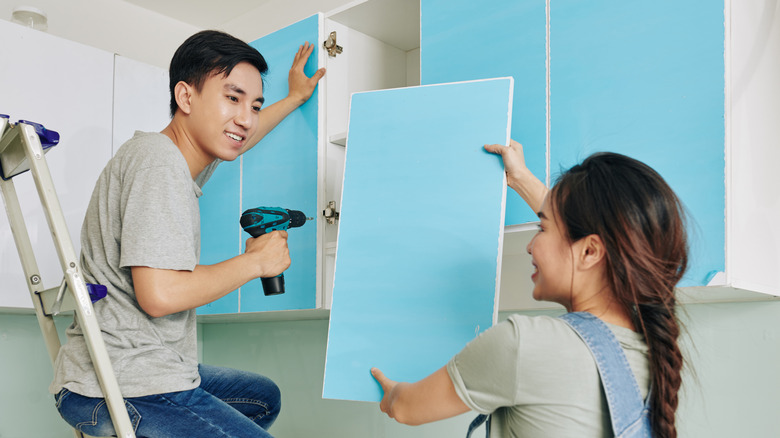 Couple installing cabinet doors in a kitchen cabinet.