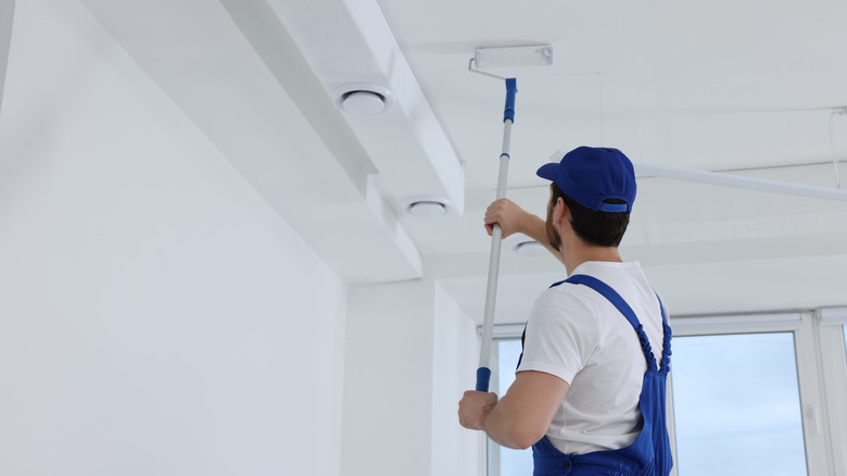 Man in painter's uniform painting white ceiling with roller