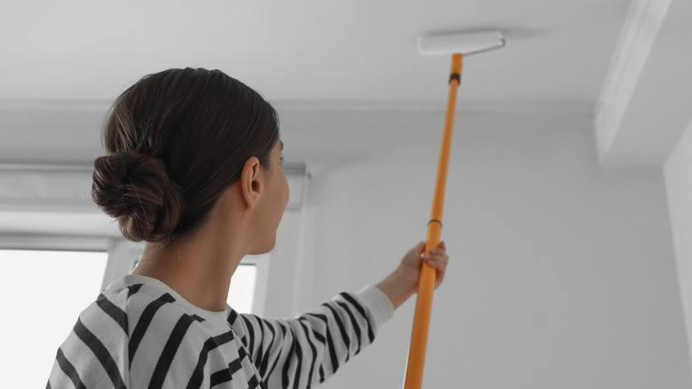 Woman in a striped shirt painting the ceiling with a roller