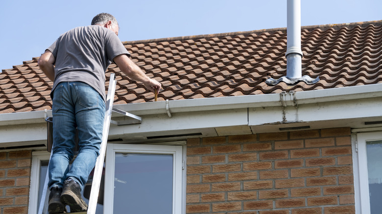 Man repairing gutter while standing on ladder