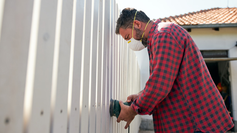 A man sands a fence while fixing it