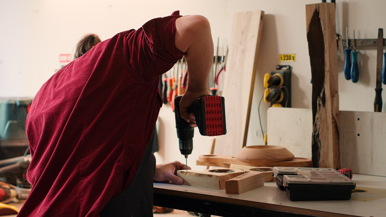 A person drilling into a piece of wood on a work bench