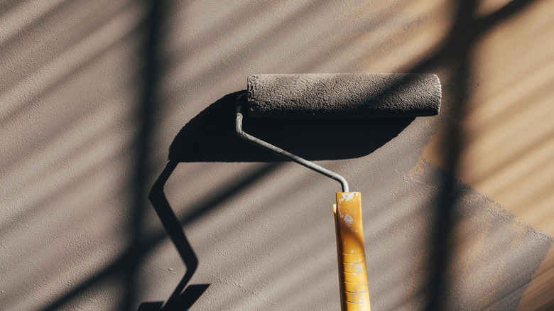 A person uses a roller to paint a living room wall brown.