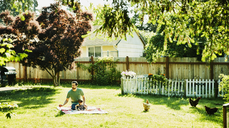 Man and infant in backyard with shady tree by fence