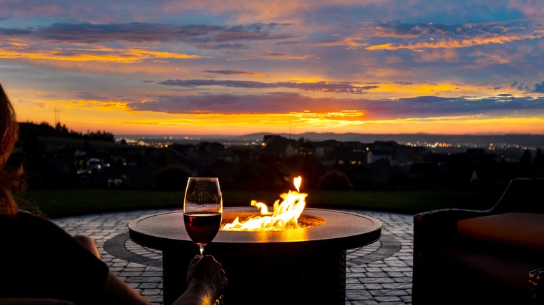 Person holding wine by firepit