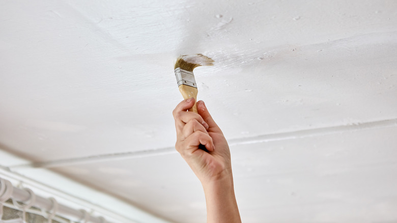 A person uses a paintbrush to touch up rough parts of a ceiling